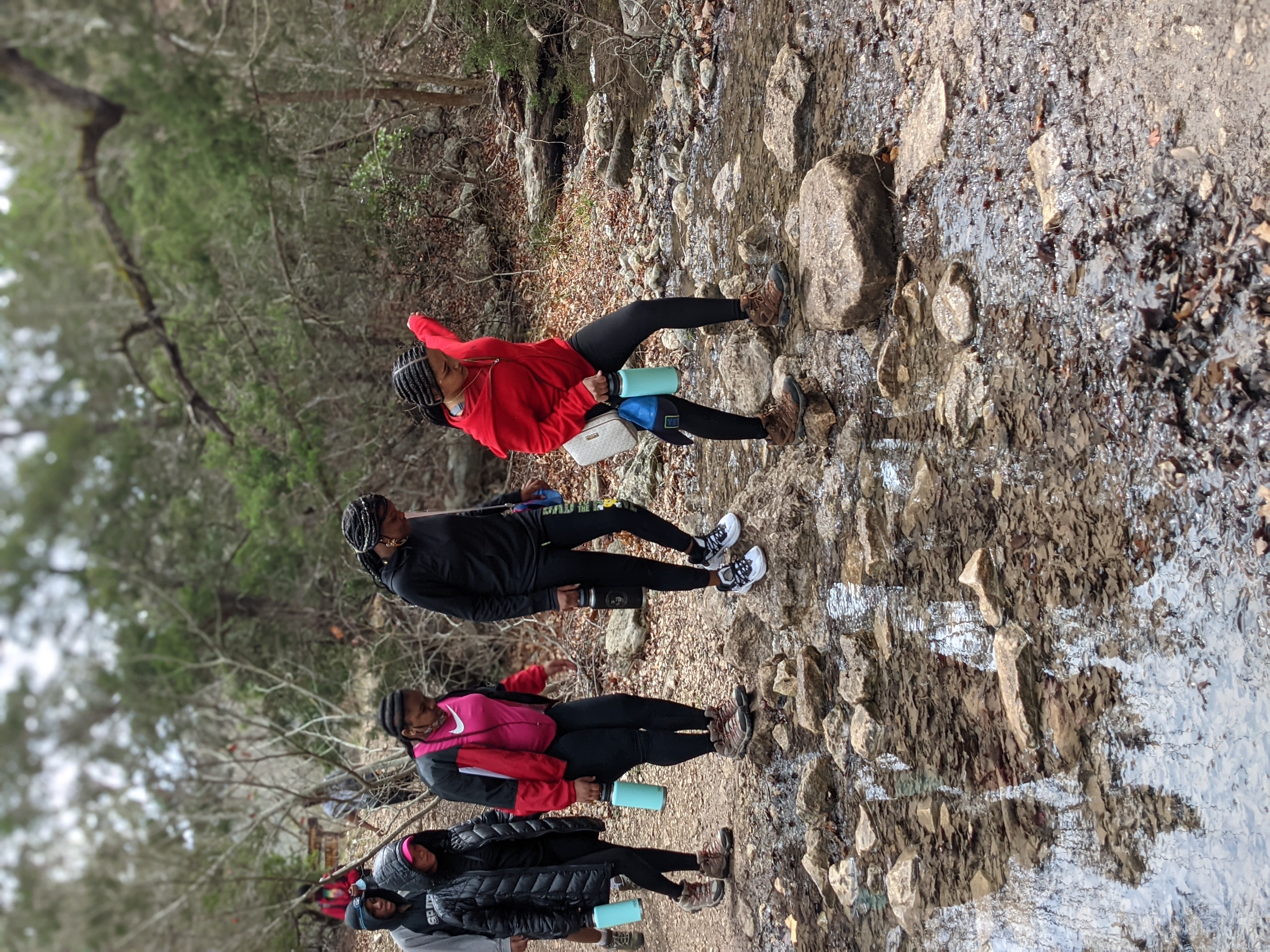 A group of hikers cross a creek in a line